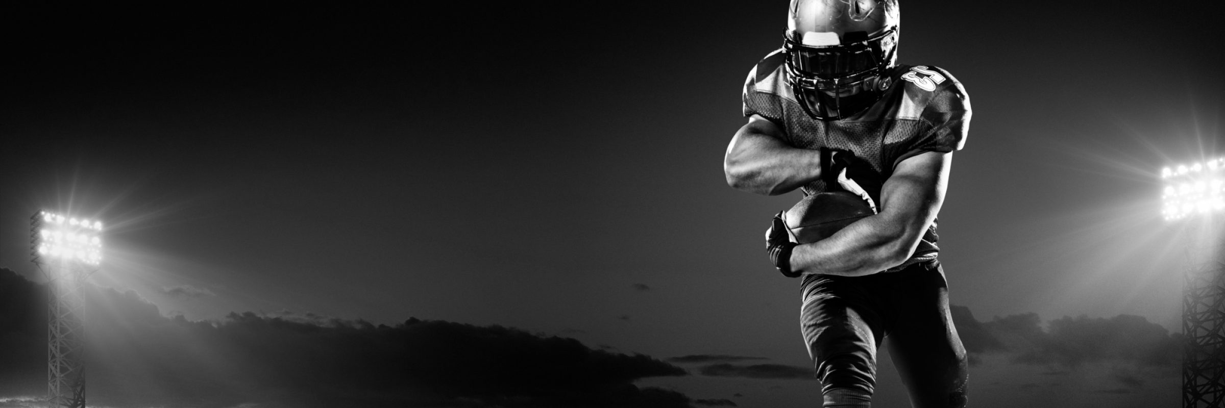 A male american football player makes a dramatic play. The panoramic view of stadium is behind him. The sky is dark and cloudy behind him.  The player is wearing generic unbranded american football uniform. The stadium is 3D rendered.